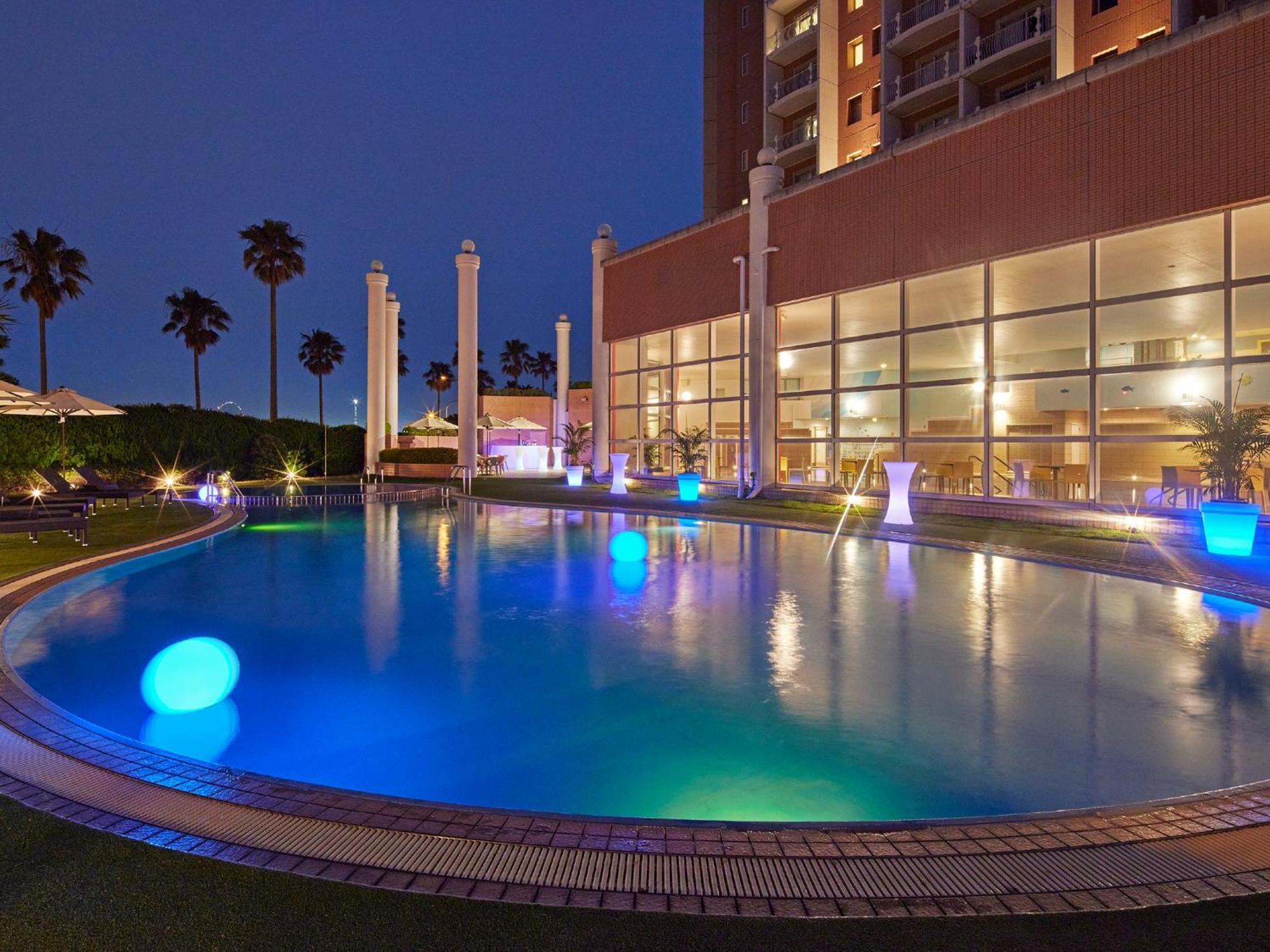 Hotel Grand Nikko Tokyo Bay Maihama Urayasu Exteriér fotografie The photo shows a well-lit swimming pool at night, surrounded by a lush green area. The pool features glowing blue lights that create a serene and inviting atmosphere. Palm trees can be seen in the background, adding a tropical feel to the scene. Add
