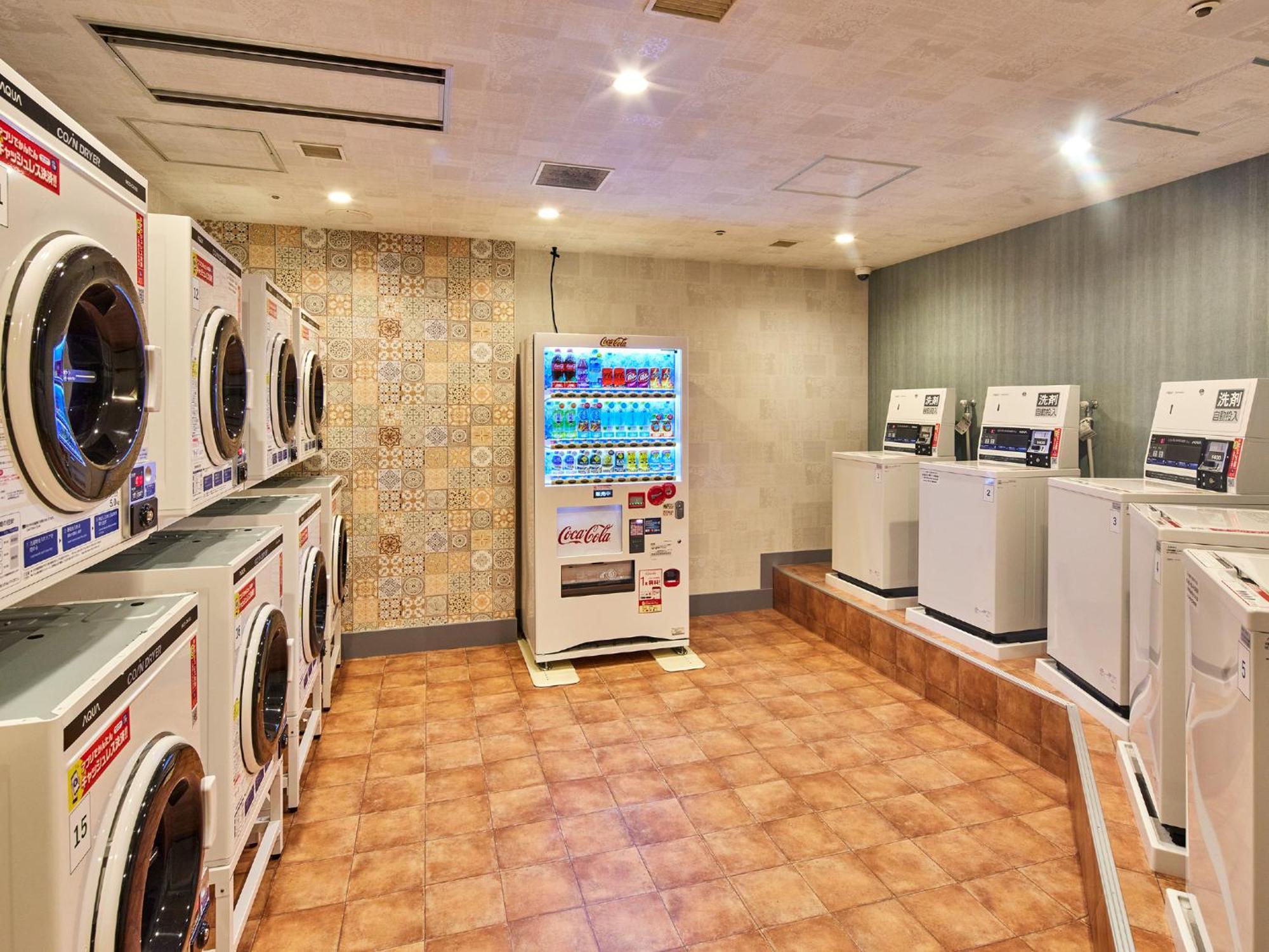 Hotel Grand Nikko Tokyo Bay Maihama Urayasu Exteriér fotografie The photo shows a laundry room equipped with several washing machines and dryers. On the left side, there are multiple front-loading washing machines arranged in a row, and on the right side, there are dryers. In the center, there is a vending machin